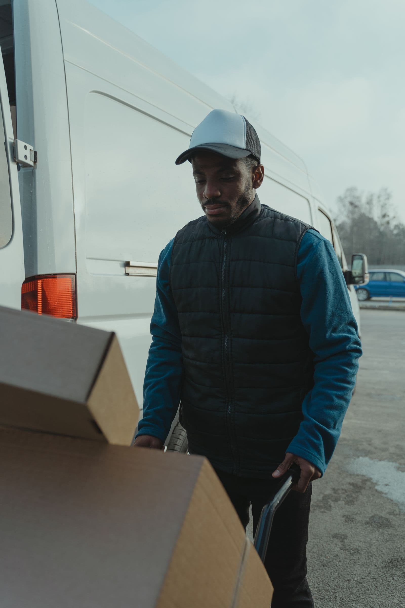 Repartidor con gorra y chaqueta acolchada cargando cajas junto a una furgoneta